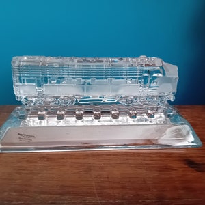 May include: A clear glass sculpture of a train engine on a glass base. The base has the text "Best Wishes" on it.