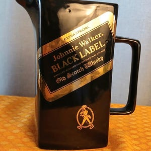 May include: Black ceramic pitcher with a handle and spout. The pitcher features a gold and black label with the text "Johnnie Walker BLACK LABEL Old Scotch Whisky". A gold emblem of a man walking is also visible.