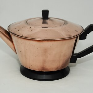 May include: A copper teapot with a black plastic handle and lid. The teapot has a black plastic base.