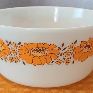 May include: White mixing bowl with an orange floral pattern. The bowl has two handles and a wide rim. The floral design features large orange flowers with brown centres and smaller orange and brown accent flowers.
