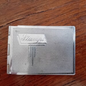 May include: A silver metal stamp album with the word "Stamps" embossed on the front cover.