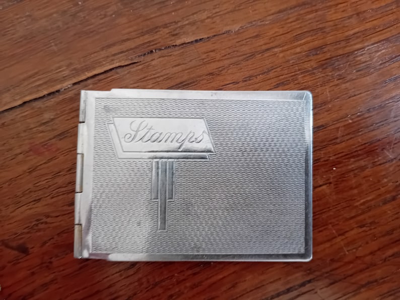 May include: A silver metal stamp album with the word "Stamps" embossed on the front cover.