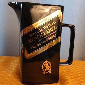 May include: Black ceramic pitcher with a rectangular handle and a pouring spout. The pitcher features a gold and black label with the text "Johnnie Walker BLACK LABEL Old Scotch Whisky". A gold emblem of a striding man is also visible.