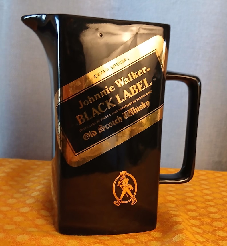 May include: Black ceramic pitcher with a rectangular handle and a pouring spout. The pitcher features a gold and black label with the text "Johnnie Walker BLACK LABEL Old Scotch Whisky". A gold emblem of a striding man is also visible.