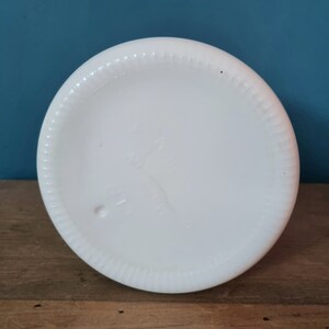 May include: The bottom of a white milk glass pitcher with a raised rim and a small mark on the bottom.