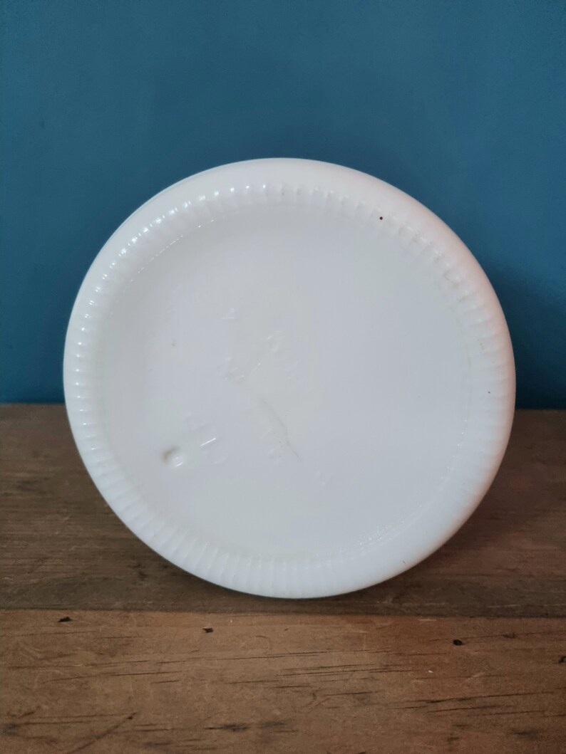 May include: The bottom of a white milk glass pitcher with a raised rim and a small mark on the bottom.