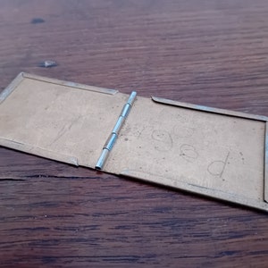 May include: A small, brass, hinged photo album with the word "aged" written on the inside cover.