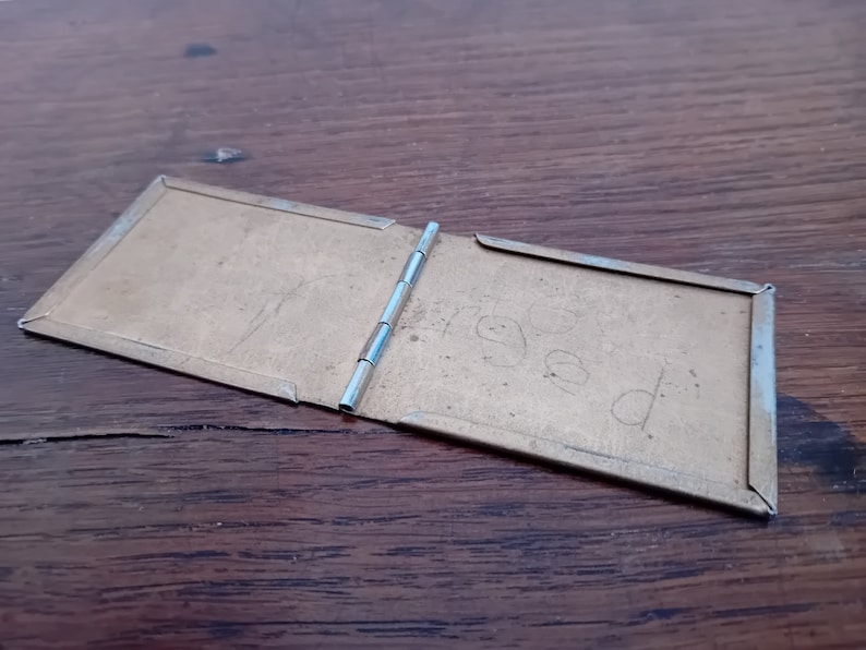 May include: A small, brass, hinged photo album with the word "aged" written on the inside cover.