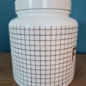 May include: White ceramic jar with a brown grid pattern and the word "Flour" printed on the side. The jar has a white lid.