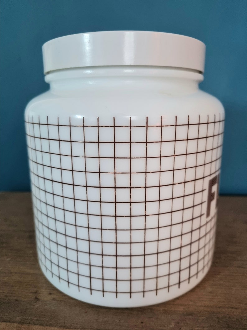 May include: White ceramic jar with a brown grid pattern and the word "Flour" printed on the side. The jar has a white lid.