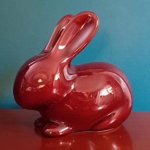 May include: A glossy, deep red ceramic rabbit figurine. The rabbit is sitting with its ears upright and its tail tucked behind it.