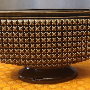 May include: A rectangular brown ceramic planter with a geometric diamond pattern. The planter has a dark brown base and rim, with small handles on each side. The textured surface adds visual interest to this decorative piece.