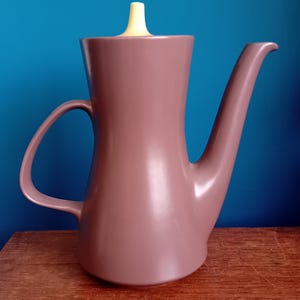 May include: A brown ceramic coffee pot with a yellow lid. The pot has a curved spout and a handle.