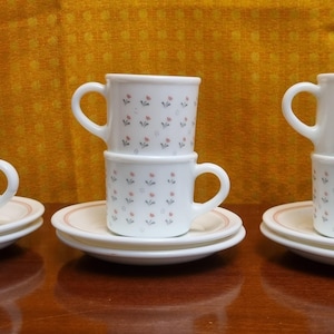 May include: Three sets of white ceramic coffee cups with a floral pattern. Each set has a saucer and three cups stacked on top of each other.
