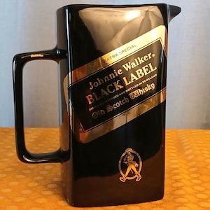 May include: A black rectangular pitcher with a handle and a spout. The pitcher features a gold and black label with the text "Johnnie Walker BLACK LABEL Old Scotch Whisky". The label also includes the text "EXTRA SPECIAL".
