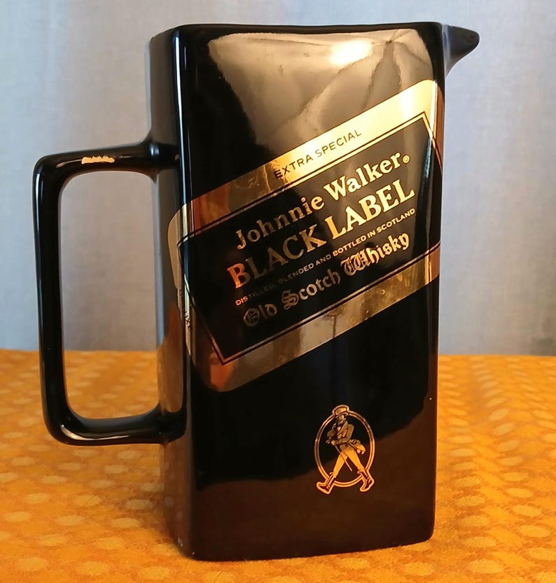 May include: A black rectangular pitcher with a handle and a spout. The pitcher features a gold and black label with the text "Johnnie Walker BLACK LABEL Old Scotch Whisky". The label also includes the text "EXTRA SPECIAL".