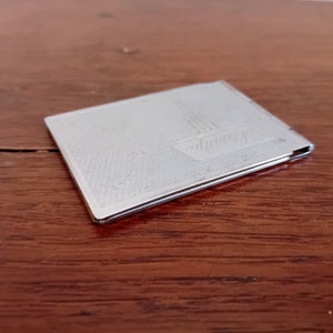 May include: A silver compact mirror with an engraved design of a ship. The mirror has a hinged lid and a smooth, reflective surface.