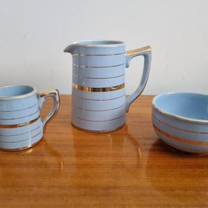 May include: A set of three blue and gold striped ceramic kitchenware pieces: a pitcher, a creamer, and a sugar bowl.