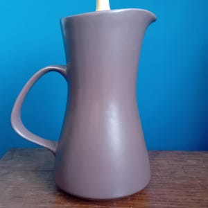 May include: A gray ceramic pitcher with a yellow lid. The pitcher has a wide base and a narrow neck. It has a handle on the side.