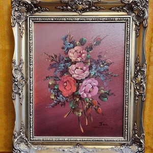 May include: A framed painting of a bouquet of pink and red roses with green leaves on a burgundy background. The painting is signed "T.M." in the bottom right corner.