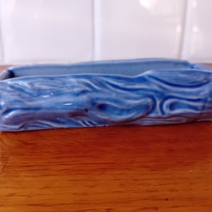 May include: A blue ceramic planter shaped like a log with a wood grain design. The planter is ideal for small plants or succulents.