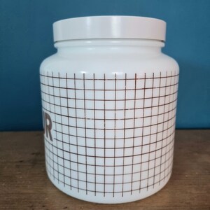 May include: White ceramic jar with a brown grid pattern and the word "Flour" printed on the side.