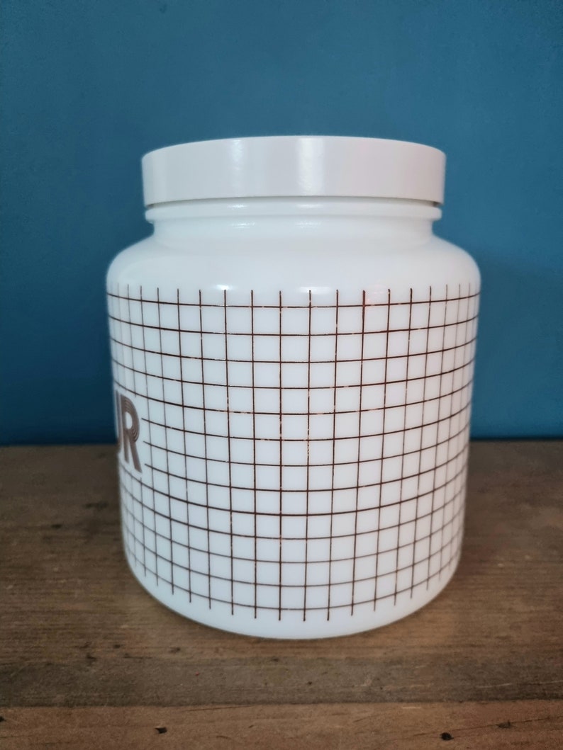 May include: White ceramic jar with a brown grid pattern and the word "Flour" printed on the side.