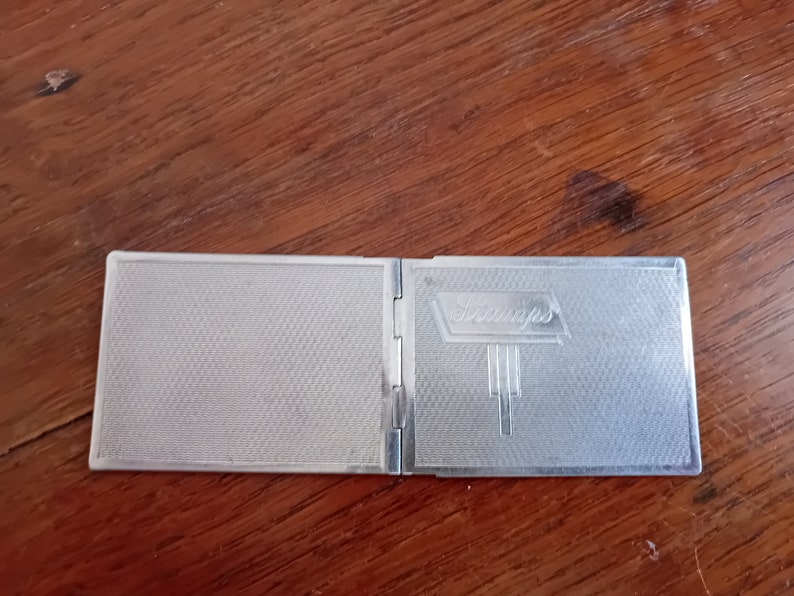 May include: A silver compact with a textured surface and the word "St. Andrews" embossed on the front.