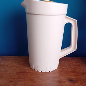 May include: A white plastic jug with a yellow lid and a handle. The jug has a strainer at the bottom.