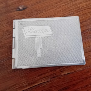 May include: A silver metal stamp album with the word "Stamps" embossed on the front cover.
