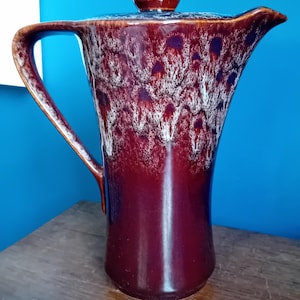 May include: A red and white ceramic teapot with a brown lid. The teapot has a unique glaze pattern with white swirls on a red background.