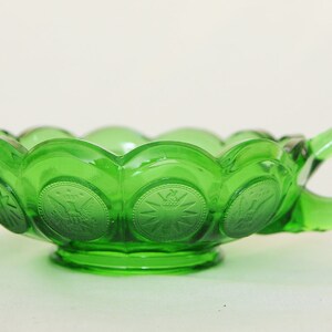 May include: A green glass bowl with a handle. The bowl is decorated with a repeating pattern of embossed coins.
