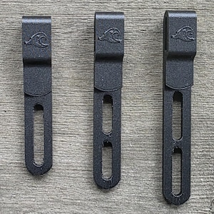 May include: Three black matte metal clips of varying lengths, each featuring a curved top hook and a vertical slotted opening. Each clip is embossed with a small wave icon near the top, providing a consistent design across all three pieces.