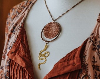 medusa. a copper necklace with an etched medusa adorned with a gold snake.