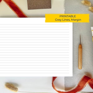 Puede incluir: Papel con líneas imprimibles con un margen gris. El papel está sobre una superficie blanca con una cinta marrón, un pequeño bloque marrón y un libro con detalles en cuero marrón.