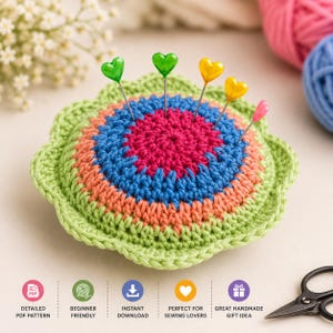 May include: A round, multi-coloured crocheted pincushion shaped like a flower with concentric rings of light green, peach, blue, and magenta yarn. Five straight pins with heart-shaped heads in green, yellow, orange, and pink are inserted into the centre.