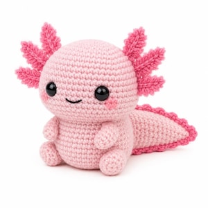 Peut inclure: Une peluche axolotl crochetée rose clair avec une grosse tête arrondie, deux yeux noirs foncés, un petit sourire brodé et deux ensembles de trois branchies externes plumeuses roses sur les côtés. Elle a une longue queue à bord festonné rose.