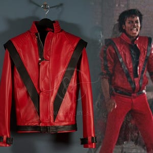 May include: A red leather jacket with black accents, hanging on a hanger. The jacket features a stand-up collar, a zipper closure, and black stripes across the chest and shoulders. The jacket is a replica of the one worn by a famous singer.