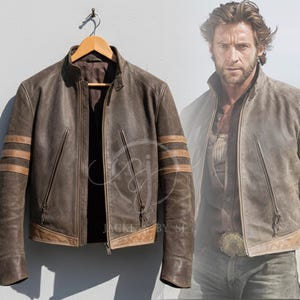 Könnte beinhalten: Eine braune Lederjacke mit Stehkragen, Frontreißverschluss und drei horizontalen beigen Streifen an jedem Ärmel. Die Jacke verfügt über zwei vertikale Reißverschlusstaschen auf der Vorderseite und einen beigen Lederbesatz am unteren Saum.