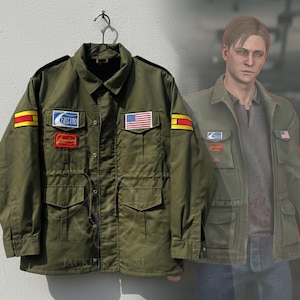 May include: An olive green jacket with multiple pockets and patches, including a US flag and text. The jacket is hanging on a black hanger. A person wearing a similar jacket is in the background.