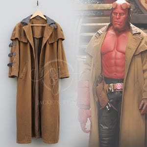 Puede incluir: Un abrigo largo marrón con un cuello ancho y múltiples bolsillos. El abrigo tiene una longitud larga y está colgado de una percha de madera. El abrigo tiene un cuello azul oscuro y hebillas marrones en las mangas.