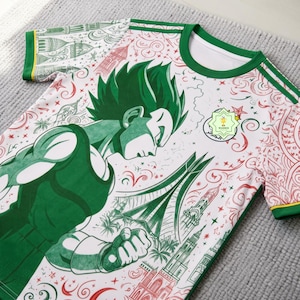 Könnte beinhalten: Ein weißes Kurzarm-T-Shirt mit einer grünen Grafik eines Anime-Charakters mit stacheligen Haaren. Das Design umfasst grüne und rote architektonische Illustrationen, Sterne und Schnörkel. Ein kreisförmiges Emblem mit einem Pokalsymbol ist vorhanden.
