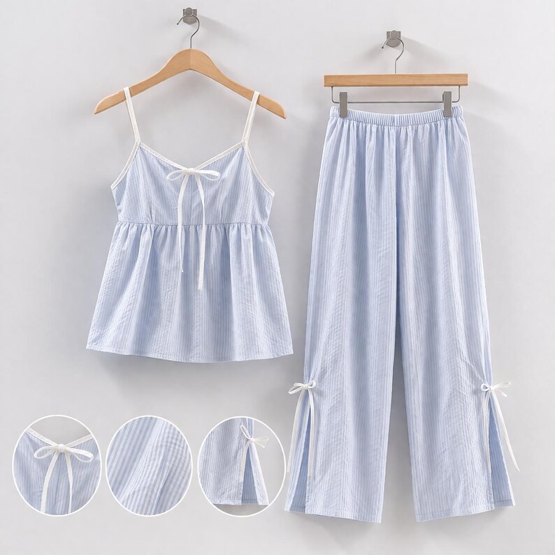 Puede incluir: Conjunto de pijama a rayas azul claro y blanco. El conjunto incluye una camiseta sin mangas con ribete blanco y detalle de lazo, y pantalones de pernera ancha a juego. Los pantalones tienen lazos en los tobillos. El conjunto de pijama est&aacute; colgado en una percha de madera.