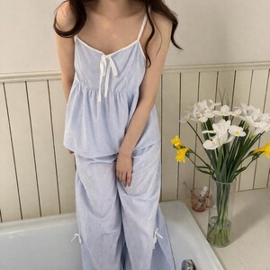 Puede incluir: Conjunto de pijama a rayas azules y blancas. El conjunto incluye una camiseta de tirantes con ribete blanco y un lazo, y pantalones de pernera ancha a juego. El pijama est&aacute; hecho de tela ligera.