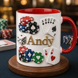 Pode incluir: Caneca de cerâmica branca com interior e alça vermelhos, decorada com fichas de poker, cartas de baralho e um dado. O nome "Andy" é exibido em letras douradas. A caneca está sobre um descanso de madeira.