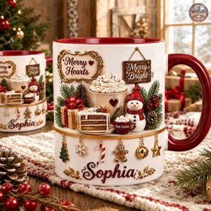 May include: A white ceramic mug featuring a 3D relief design of a snowman, a slice of cake, a gift box, and a cup of hot cocoa. The mug displays the text Merry Hearts and Merry & Bright, with the name Sophia in gold script and hanging ornaments.