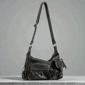 May include: Black leather shoulder bag with multiple exterior pockets and a long adjustable strap. The bag features silver-tone hardware, including D-rings and buckles. The bag has a zippered main compartment and several smaller pockets.