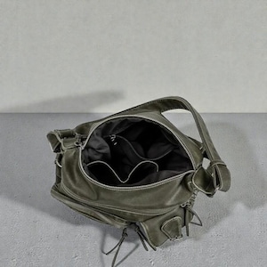 May include: Olive green shoulder bag with multiple compartments and a zipper closure. The bag has a top handle and two exterior pockets with zipper closures. The interior is black.