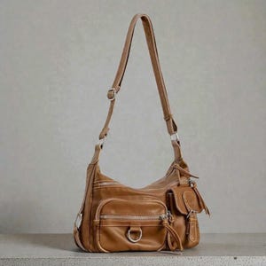 May include: A brown leather shoulder bag with multiple exterior pockets and silver-toned hardware. The bag features a long, adjustable strap and a zip closure on each pocket. The bag has a tassel detail on one of the pockets.