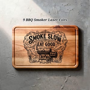 Puede incluir: Tabla de cortar rectangular de madera con esquinas redondeadas. Presenta un grabado negro detallado de un ahumador con el texto "SMOKE SLOW EAT GOOD" rodeado de humo y adornos decorativos. El texto "9 BBQ Smoker Laser Files" está en la parte superior.